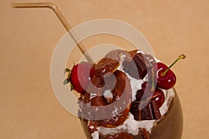 Close up of chocolate indulgent extreme milkshake with brownie cake, strawberries, cherries, and a plastic straw with