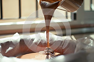 A close-up of chocolate milk liquid being poured into the form of a confectionery syringe in the form mold or mould. Preparation