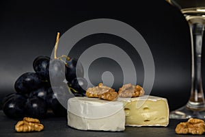 Close-up chopped camembert cheese, nuts and sweet blue grapes on the background of a glass of white dry wine