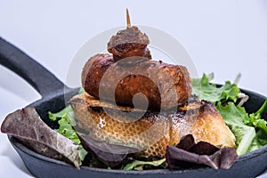 Close up of a chorizo tapa with green leaves on a iron skillet