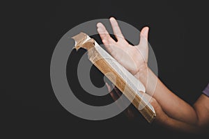 Close up of christian woman hand holding holy bible pray and worship for thank god in church with black background, adult female