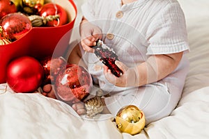 Close-up Christmas Baby in Santa Hat, Child holding christmas bauble near Present Gift Box over Holiday Lights