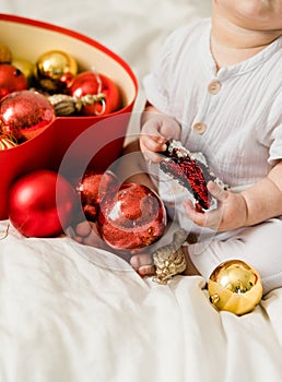 Close-up Christmas Baby in Santa Hat, Child holding christmas bauble near Present Gift Box over Holiday Lights