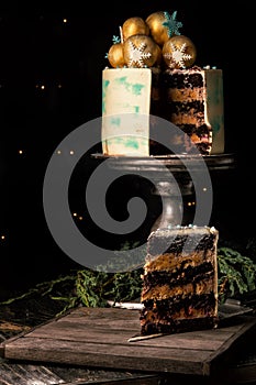 Close up. Christmas cake in the cut. Nearby is a wooden board with a piece of sliced chocolate cake and juniper branches.
