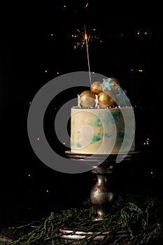 Close up. Christmas cake and one burning sparkler festively decorate it. Dark background with christmas lights