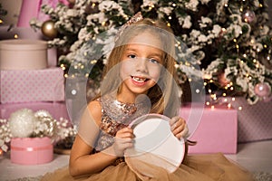 Close up. Christmas concept. A beautiful little girl in an elegant dress sits and smiles while holding a pink gift box