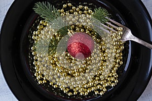 close up of christmas decorations, gold beads, fir tree branches and red christmas ball in black plate like italian