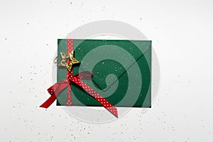 Close-up of Christmas envelope of green color decorated with star toy, red ribbon and glitter, isolated on white background.