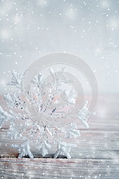 Close-up Christmas toy snowflake is standing on wooden table on light grey background with snow.