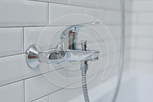 Close-up of chrome shower, faucet, in the bathroom covered decorative ceramic tiles with white glossy bricks.