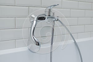 Close-up of chrome shower, faucet, in the bathroom covered decorative ceramic tiles with white glossy bricks.