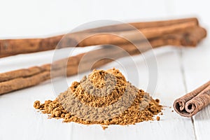 Close-up of cinnamon powder and cinnamon sticks on white wood