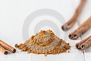 Close-up of cinnamon powder and cinnamon sticks on white wood