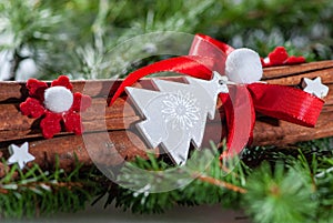 Close-up cinnamon sticks on sprigs of green spruce with a white wood christmas tree with red ribbon, snowflakes and white stars