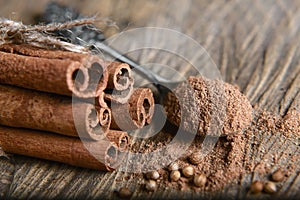 Close-up cinnamon sticks tied and ground cinnamon on a spoon of cardamom seeds on wooden background, macro