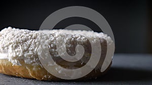 Close-up circling around shot of tasty white donut with coconut chips spinning slowly on gray table background.