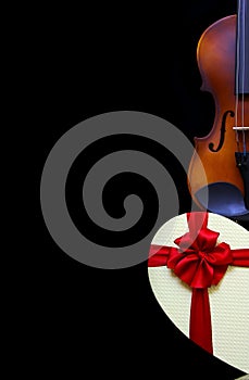 Close up of a classic violin and a heart shape gift box with a red ribbon bow