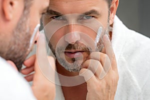 Close-up clean man face. Matured man applying cosmetic cream on face. Facial treatment. Beauty portrait of man applying