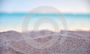 Close up of clean yellow sand surface covering seaside beach with blue sea water on background. Travel and vacations