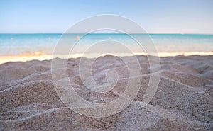 Close up of clean yellow sand surface covering seaside beach with blue sea water on background. Travel and vacations