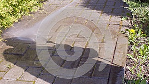 Close up cleaning roadway brick with high pressure water jet washing off moss