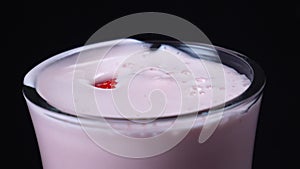 Close-up of clear glass of strawberry milkshake with large red fallen strawberry on the black background. Frame