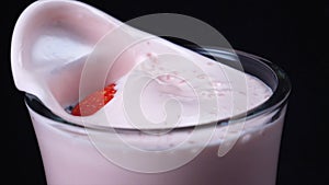 Close-up of clear glass of strawberry milkshake with large red fallen strawberry on the black background. Frame