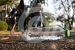 Close up clear plastic bottle water drink with a green cap on the road in the park at blurred background