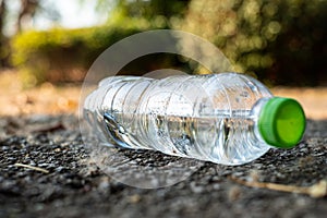 Close up clear plastic bottle water drink with a green cap on the road in the park at blurred background, Trash that is left