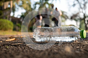 Close up clear plastic bottle water drink with a green cap on the road in the park at blurred background, Trash that is left