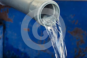 Close-up of clear water flowing out of a pvc pipe hole. The concept of water supply, water consumption.