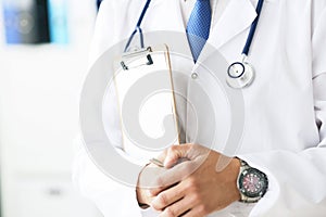 Close-up of clipboard with blank paper in medical doctor hand. Male doctor listens to the patient holding a clipboard