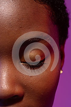 Close up of closed eye of african american woman with short hair on purple background