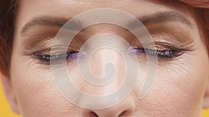 Close up of closed eyes with purple and gold eyeshadow of mature red hair woman