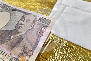 Close-up on cloth masks and 100,000 yen in cash on a golden paper.
