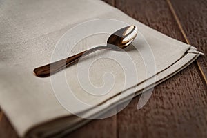Close up of cloth napkin of beige color and served tea spoon on wooden table