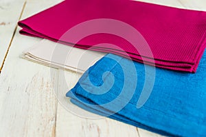 Close up of cloth napkins of beige, blue and burgundy colors on rustic white wooden table. Shallow depth of field