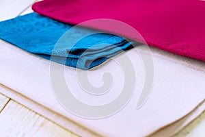 Close up of cloth napkins of beige, blue and burgundy colors on rustic white wooden table. Shallow depth of field