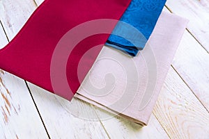 Close up of cloth napkins of beige, blue and burgundy colors on rustic white wooden table. Shallow depth of field