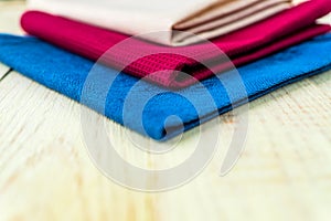 Close up of cloth napkins of beige, blue and burgundy colors on rustic white wooden table. Shallow depth of field