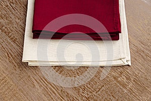 Close up of cloth napkins of beige, and burgundy colors on rustic brown wooden table