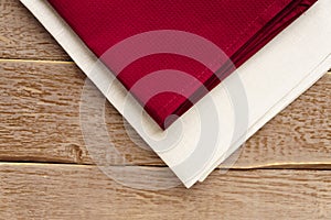 Close up of cloth napkins of beige, and burgundy colors on rustic brown wooden table