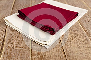 Close up of cloth napkins of beige, and burgundy colors on rustic brown wooden table. Shallow depth of field