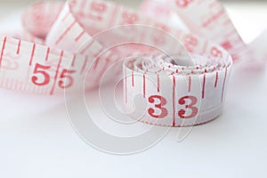 Close-up cloth tape measure with red numbers rolled up on white background. Body measure with inches