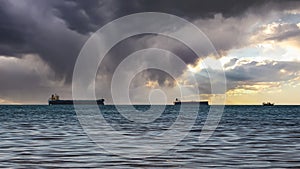 Close-up of a cloudy seascape and a bright sunset. Blue sea, storm clouds with sun rays over the horizon, and several cargo ships