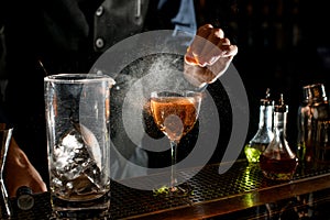 Close-up of cocktail glass which bartender sprinkling by juice of citrus.