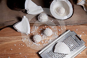 Close up of coconut with white pulp, grater with coconut chip and white candies on wooden background