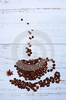 Close- up of coffee beans in the form of a cup, saucer and steam on a light wooden background. Vertical