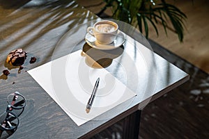 Close up of coffee cup, cookies, glasses, blank sheet of paper and pen on table