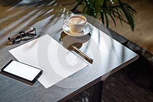 Close up of coffee cup ,glasses, paper, pen and mobile phone with blank screen.